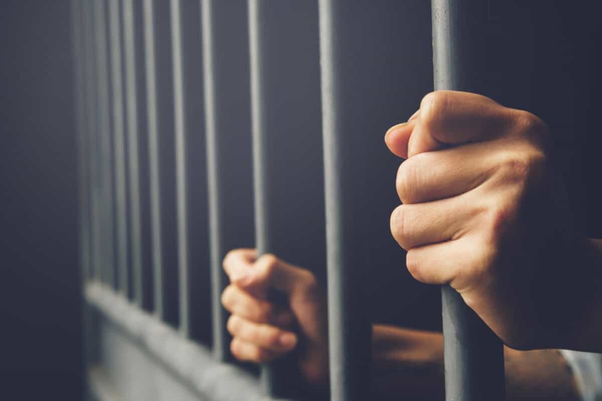 Closeup of hands holding bars of a jail cell