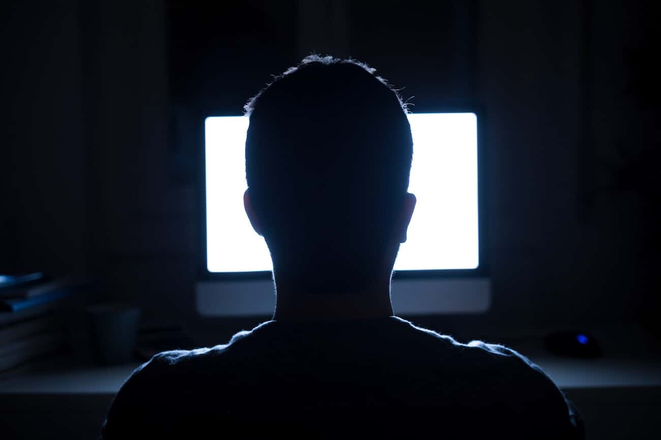Silhouette of man's head in front of computer monitor at night