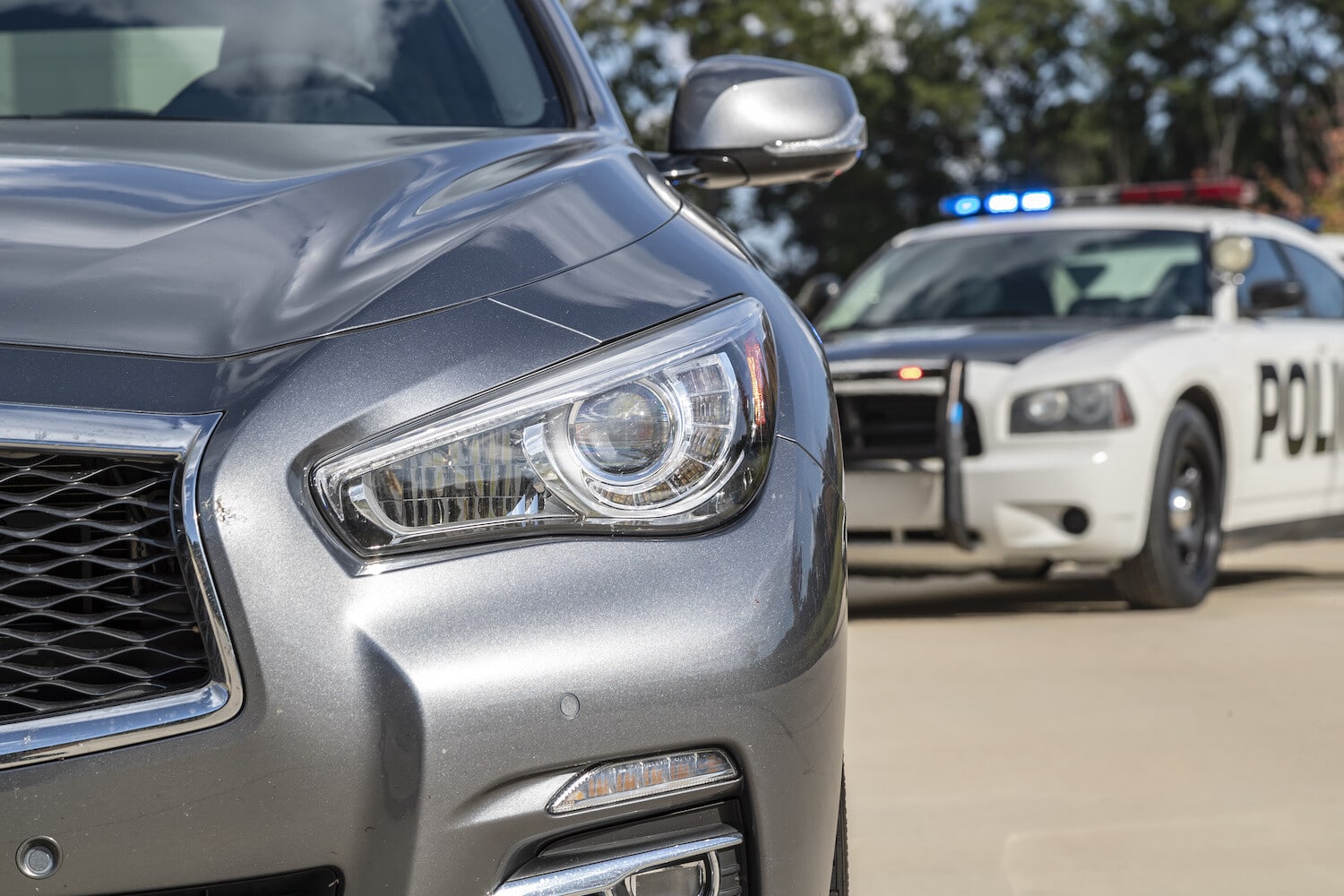 Silver car parked with police cruiser behind it at a traffic stop.