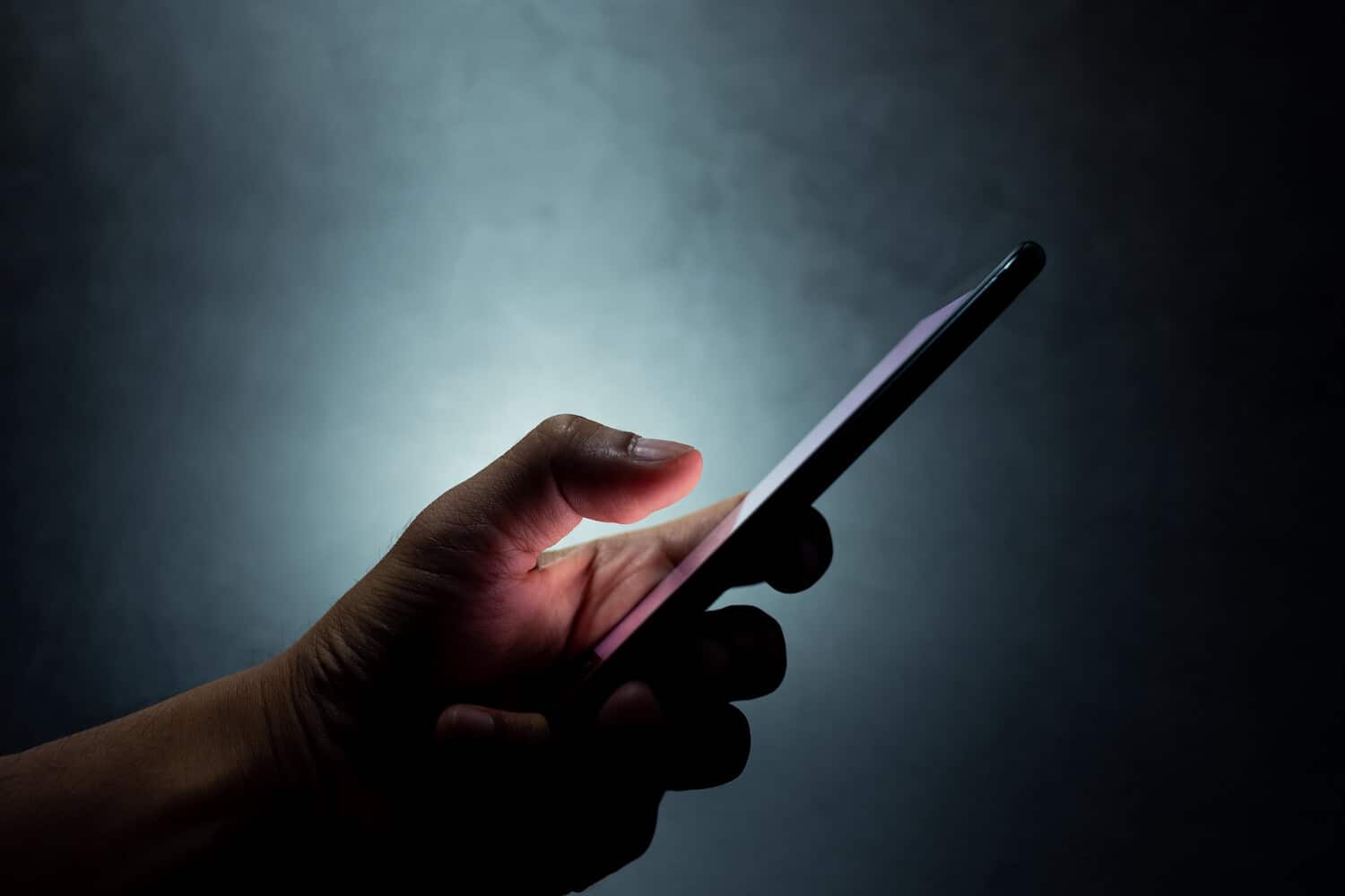 silhouette of a hand holding a mobile phone in darkness
